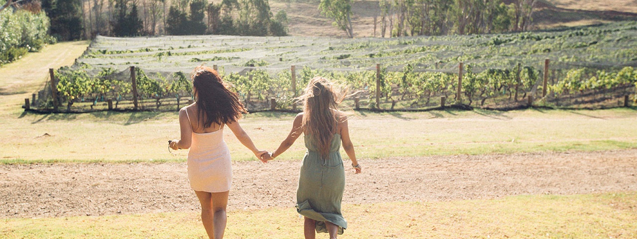 Stonyridge Vineyard Two girls holding hands walking towards the vines at Stonyridge Vineyard on Waiheke Island